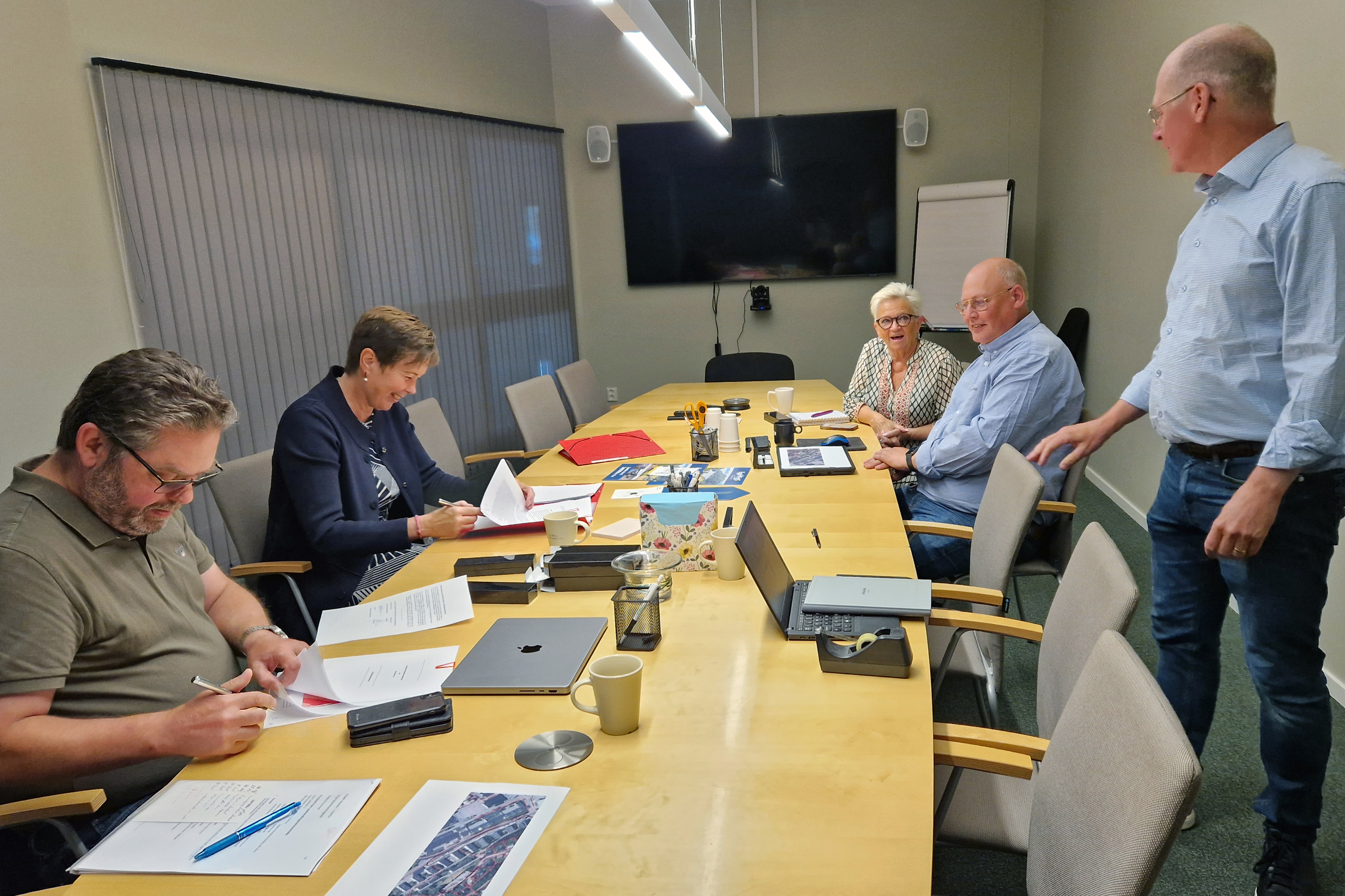 tre personer står i ett rum, två skakar hand